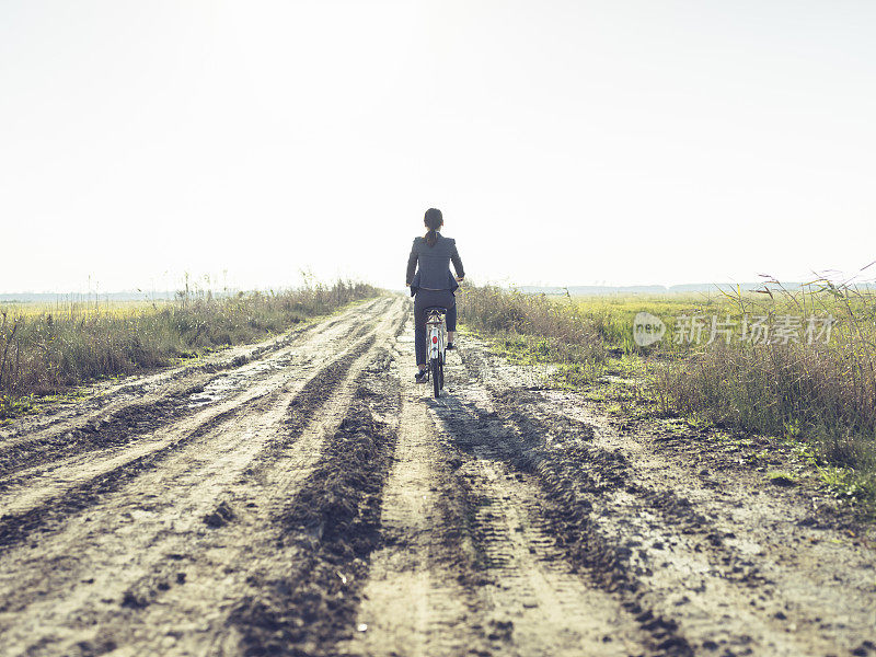 一个阳光明媚的日子里，年轻的女商人骑在乡间小路上