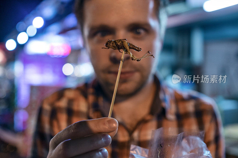 泰国夜市上吃蟋蟀的白人年轻男子。