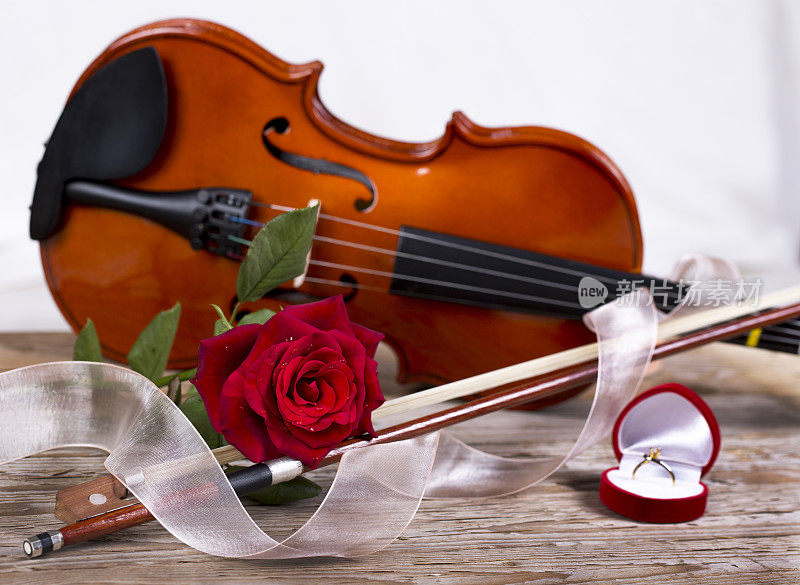 木桌上放着金戒指、红玫瑰和小提琴