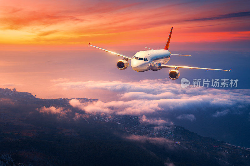 乘飞机。风景与大白色飞机是飞行在天空的云彩和海上在彩色日落。客机在黄昏时分降落。商务旅行。商用飞机。旅行