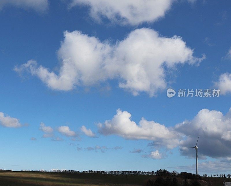 在乡村环境中，蓝天映衬着蓬松的白云，还有风力涡轮机或乡村公路