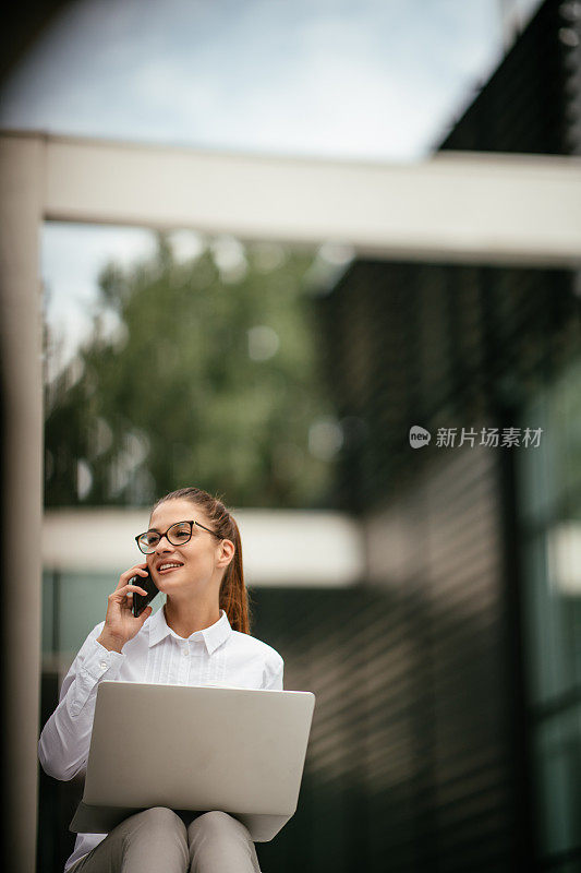 年轻漂亮的女商人一边打电话一边喝咖啡