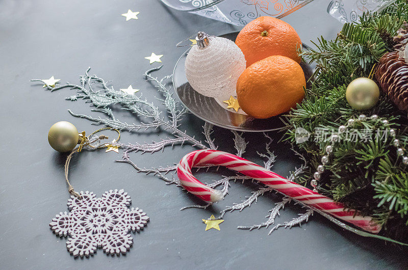 用松果、圣诞装饰品、彩带和冷杉枝制作的节日手工花环，在黑色背景上点缀新鲜的橘子