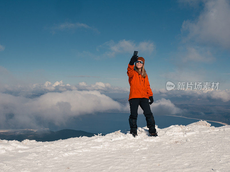 冬季日出时，女性高山攀登者在高海拔的山峰上竖起大拇指