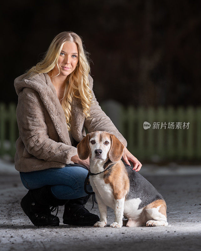 一个金发年轻女人和她的小猎犬在冬天的街道上