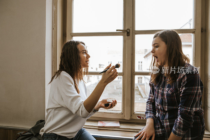 两个十几岁的女孩在靠近窗户的教室里化妆