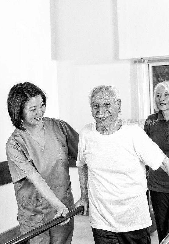 微笑的亚洲理疗师协助病人行走在双杠之间