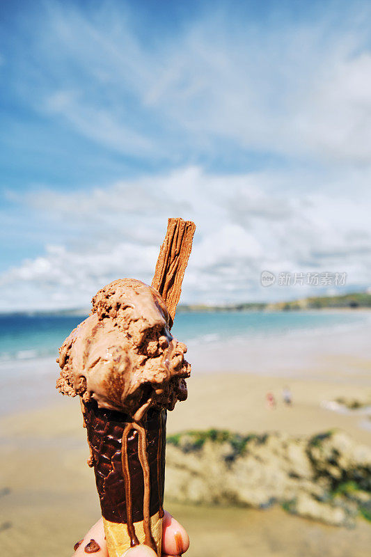 6月的一个阳光明媚的日子里，康沃尔纽基的托万海滩上，手拿着巧克力冰淇淋。