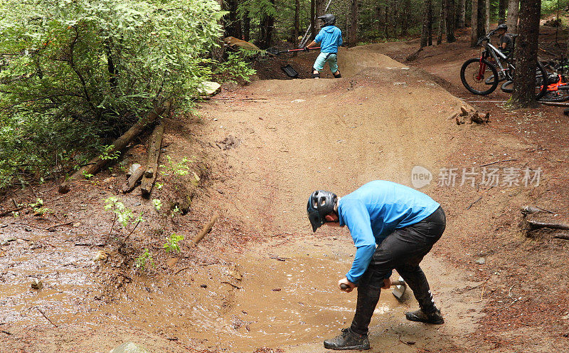 在雨林中，两名山地自行车手用铲子把自行车道上的水铲掉