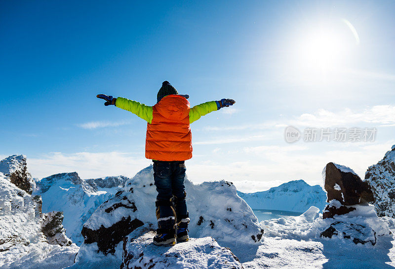 一个小男孩在雪山顶上举起他的手臂