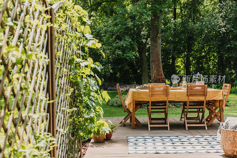 铺着橙色台布的餐桌矗立在绿色花园的木质露台上