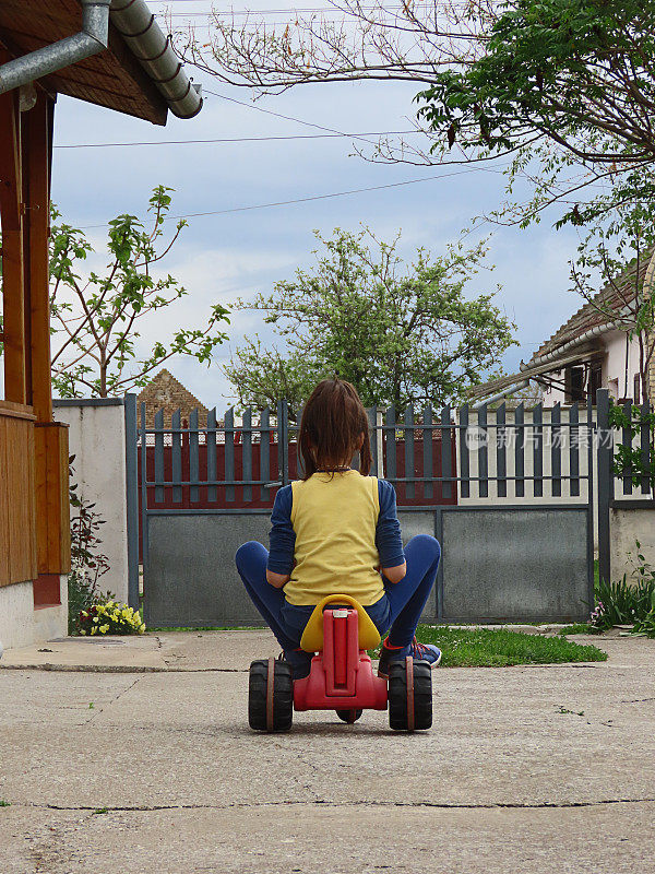 小女孩在后院开着一辆塑料玩具三轮车