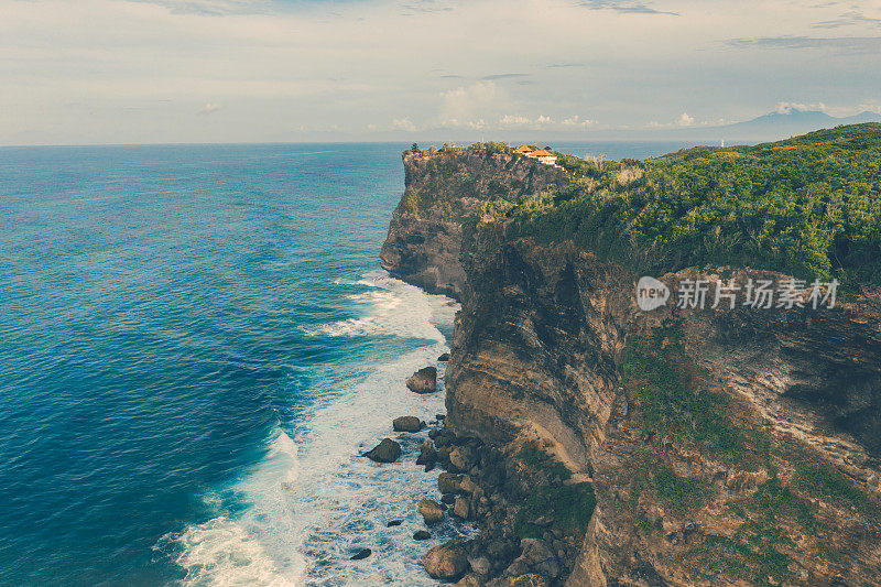 Uluwatu巴厘岛。蓝色的海洋和岩石山，覆盖着热带树木。