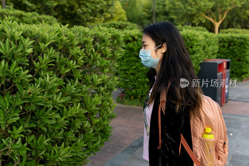 亚洲女学生背包戴防护医疗口罩。在冠状病毒关闭后，的学校将重新开学。