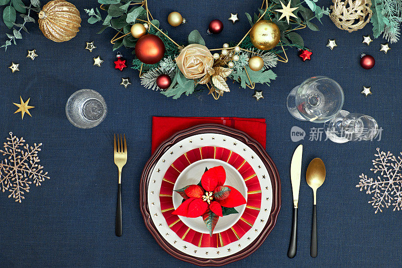 圣诞餐桌设置在金色，酒红色和经典的蓝色。俯视图的装饰餐桌布局，金色的餐具，白色的盘子与星星。传统的圣诞节装饰在经典的蓝色亚麻布上