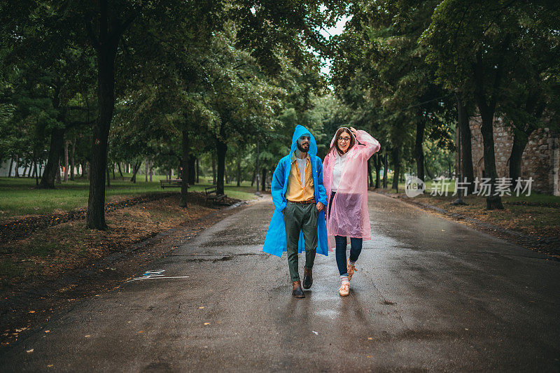 快乐的年轻夫妇在雨中在公园里穿着雨衣