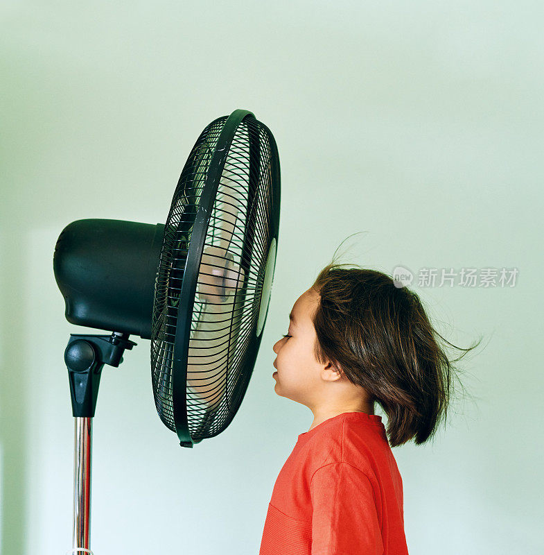 在炎热的夏日里，可爱的孩子站在电风扇前
