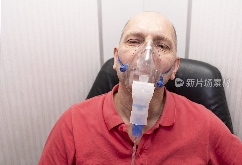 一个40到50岁的白人男性，用喷雾器吸入。人像，男人的眼睛是闭着的。