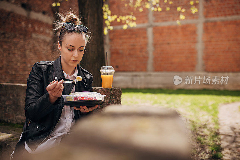 年轻女子在公园里吃着新鲜的有机沙拉，喝着橙汁