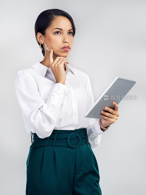 一个年轻的女商人正在用一个数码平板电脑，在灰色的背景下看起来很有思想