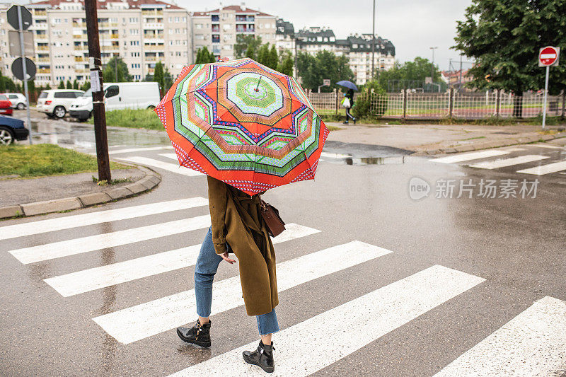 女性行人撑着雨伞在雨天过马路