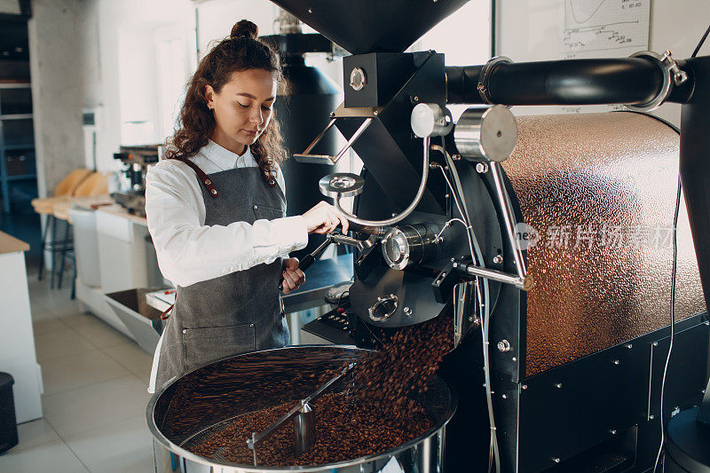 在咖啡烘焙过程中，咖啡在烘培机上冷却。年轻的女咖啡师正在搅拌咖啡豆。