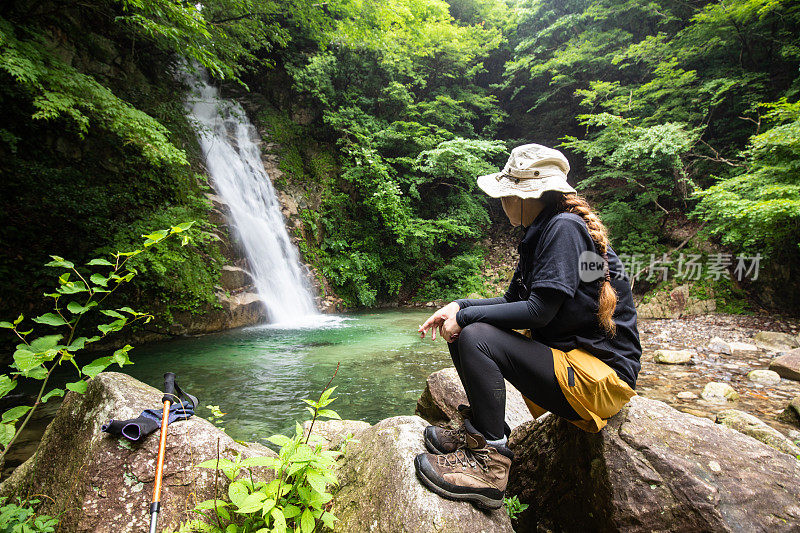 女徒步旅行者在瀑布边抽着烟休息