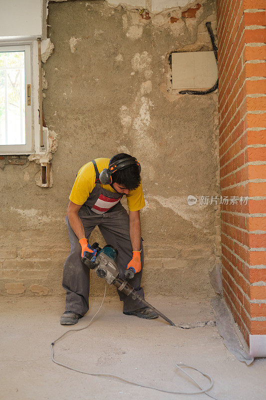 年轻的建筑工人用手提钻拆房子的地板。