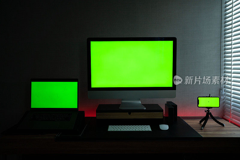 客厅的书桌上放着显示绿色色度按键屏幕的笔记本电脑和智能手机。