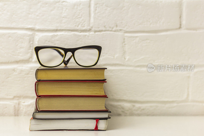 桌上有一堆厚厚的精装书和矫正眼镜。阅读和学习用的小说或教育文学。