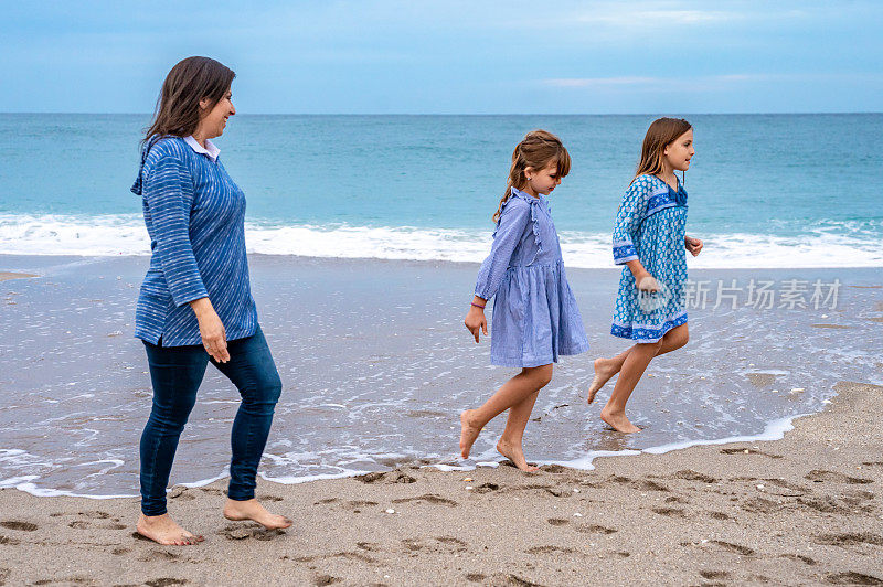 拉丁裔母亲，带着孩子的家人一起漫步在田园诗般的海滩上
