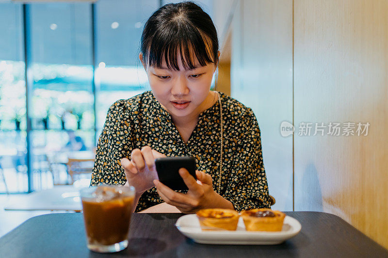 亚洲女性在咖啡馆喝咖啡，使用智能手机