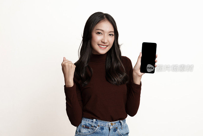惊讶的年轻亚洲女子站在白色背景下，拿着智能手机。