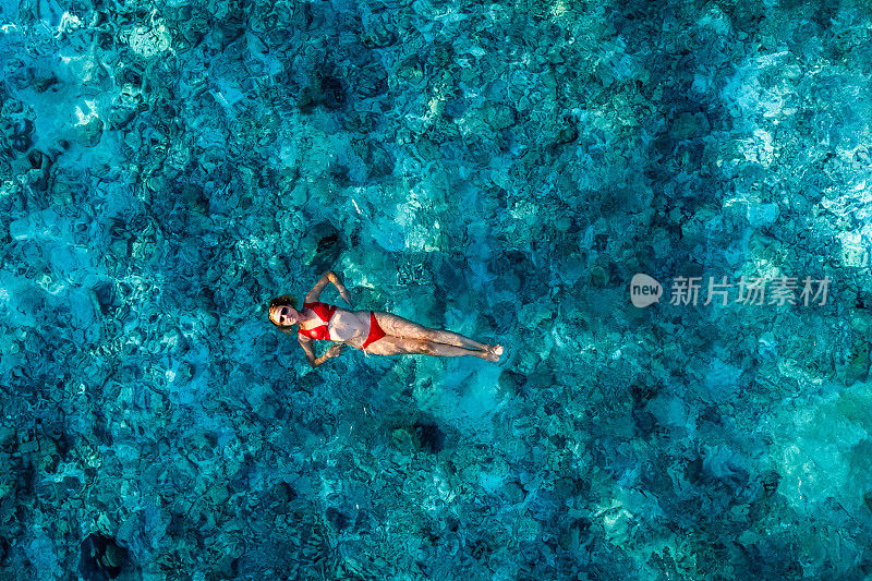 一个女人躺在海洋里礁石上晶莹的水面上