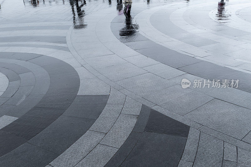 行人在被雨水淹没的广场上留下倒影