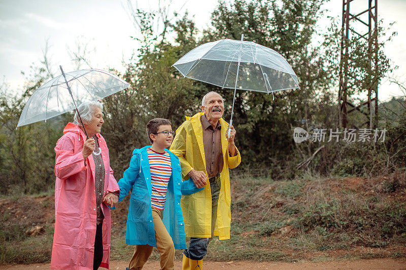 快乐的几代同堂在雨天的大自然中打着伞散步