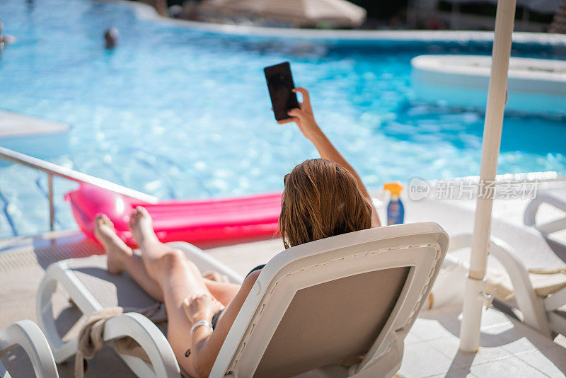 女旅行者放松和自拍的手机在酒店的游泳池，而暑假