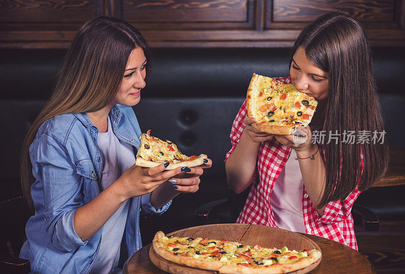 两个十几岁的女孩在一家餐厅享受美味的披萨