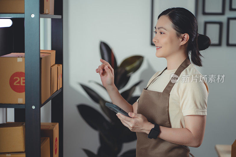 亚洲女性在线卖家使用智能手机，在家中办公室查看库存产品。