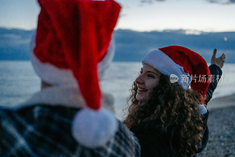 希腊，一对戴着圣诞帽的年轻夫妇在黎明时分欣赏着海岸线的景色