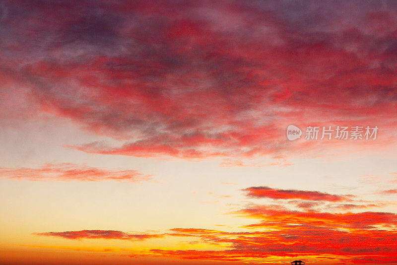 美丽日落的纹理背景。令人惊叹的红色和黄色日落与燃烧的云全景日落云景戏剧性的天空。晚霞，光在云中反射
