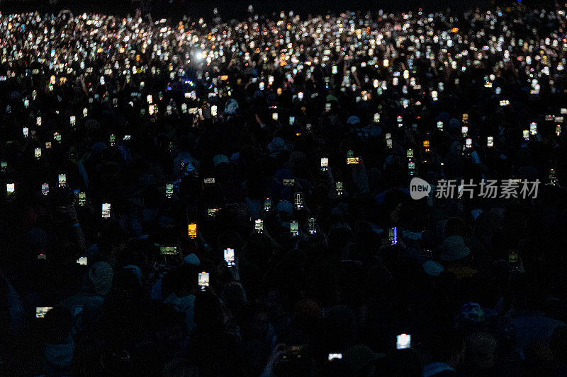 一场夜间音乐会，人们把手机举在空中，远离镜头，朝向舞台