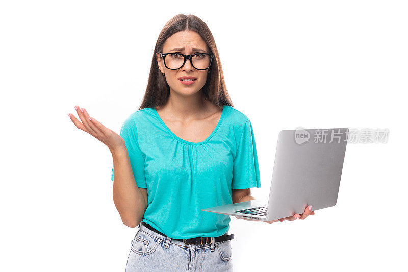 年轻迷人的欧洲女人，黑色长发，穿着蓝色t恤，正在用笔记本电脑远程学习