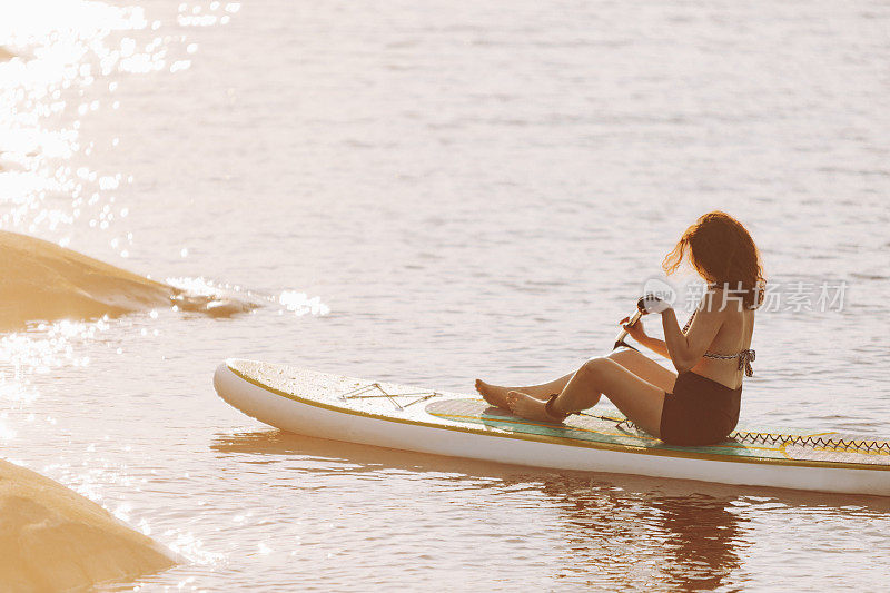 一个中年妇女在日落时分在湖边玩桨板