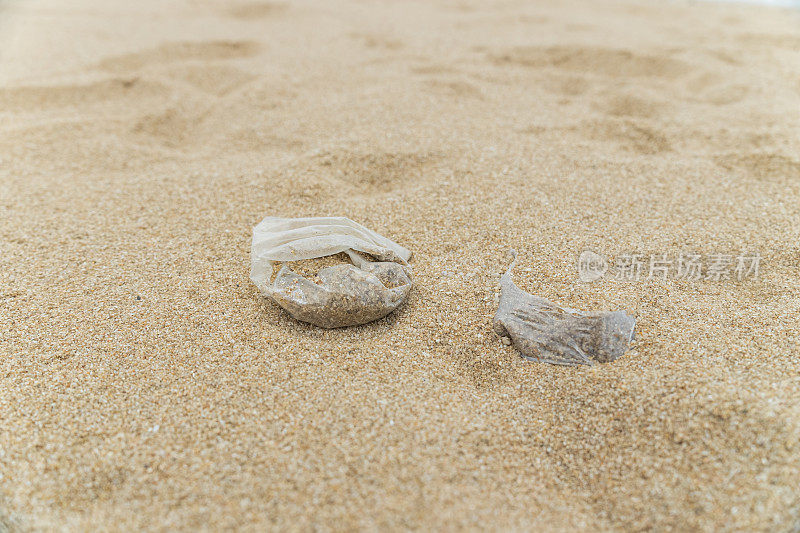 塑料袋嵌在沙滩上，造成人为造成的塑料污染。塑料污染导致环境清理，以改善人类和海洋生物的环境和社会问题。