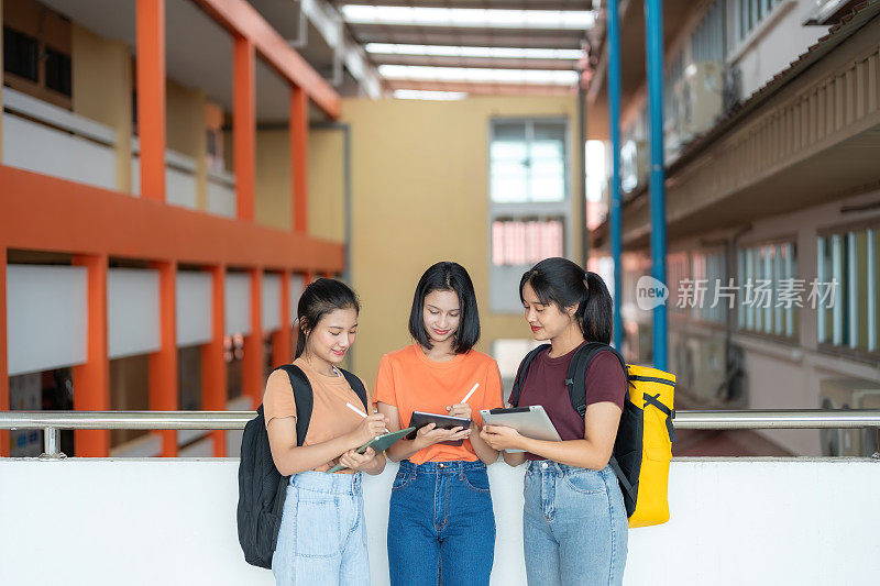 广角镜头，三名女学生站在国际学院大楼里，拿着笔记本电脑开会。在名牌大学里，穿休闲装，背书包。