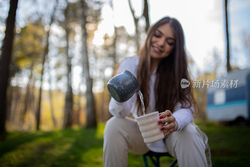 年轻女子正在用杯子给她倒水，她正在大自然中煮咖啡