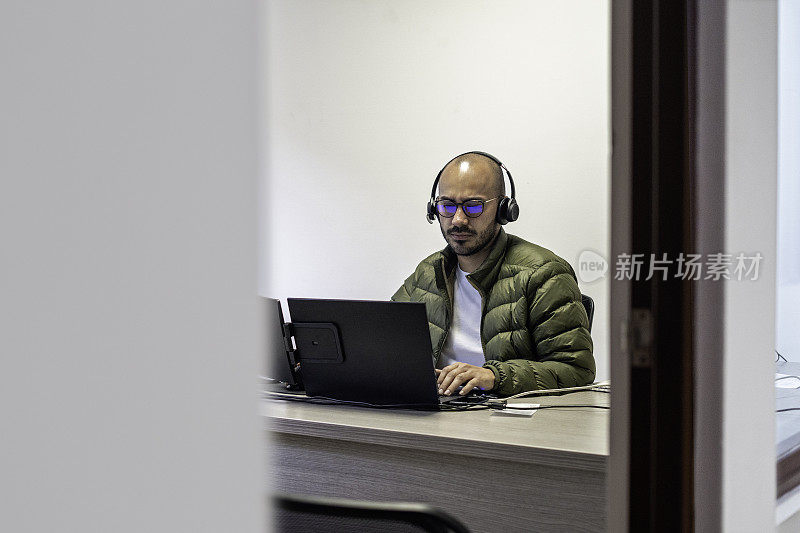 在呼叫中心工作的人的肖像，在办公室里拿着笔记本电脑和耳机麦克风。