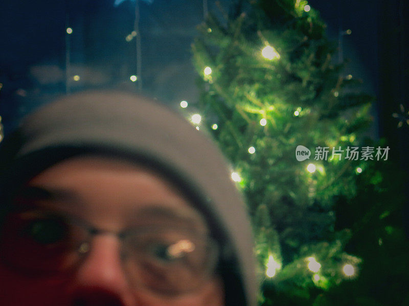 戴着眼镜和帽子的炸弹客在圣诞树前拍照