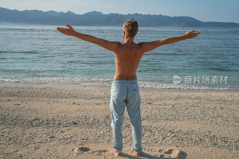 年轻人在海滩上伸开双臂享受热带气候和异国情调的假期。旅游目的地自由的人好奇的概念自然